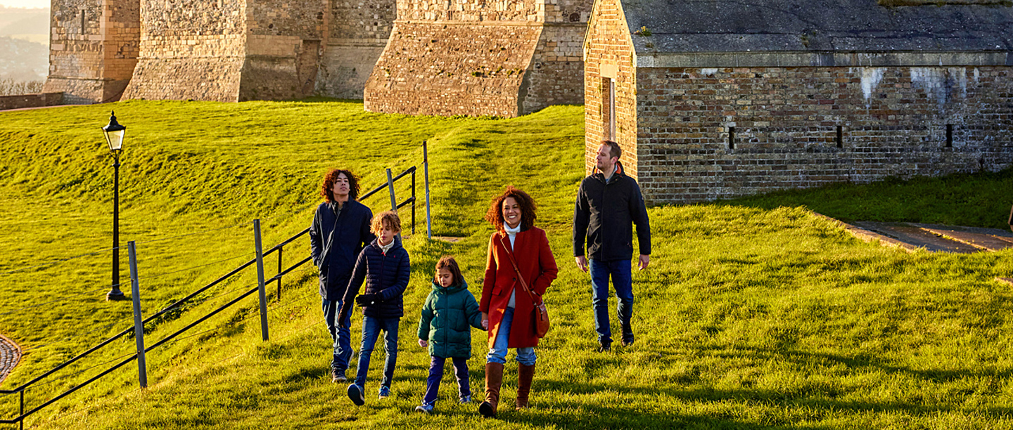 A group of two adults and three children walking next to Dover Castle. They are dressed in coats and winter clothing.