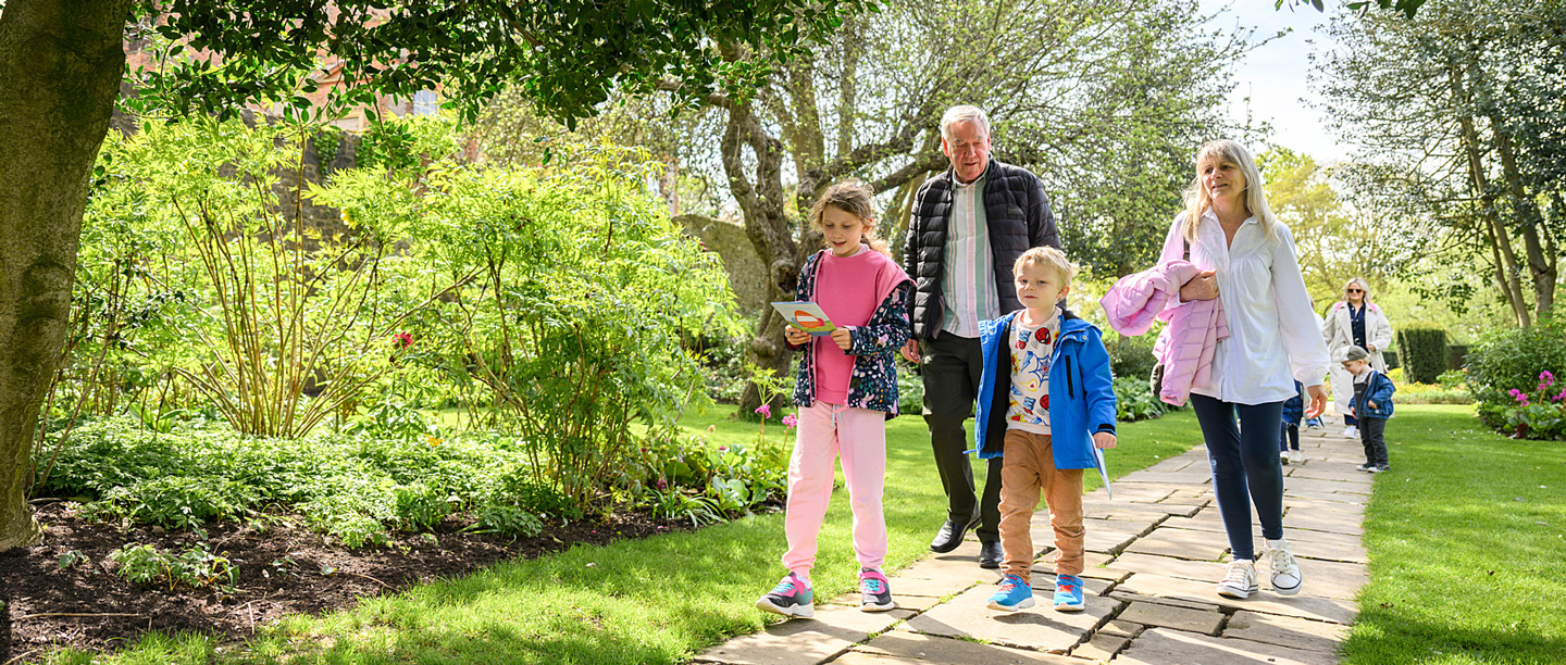 An older couple walk along a path with two young children at Eltham Palace, taking part in an Easter Quest.