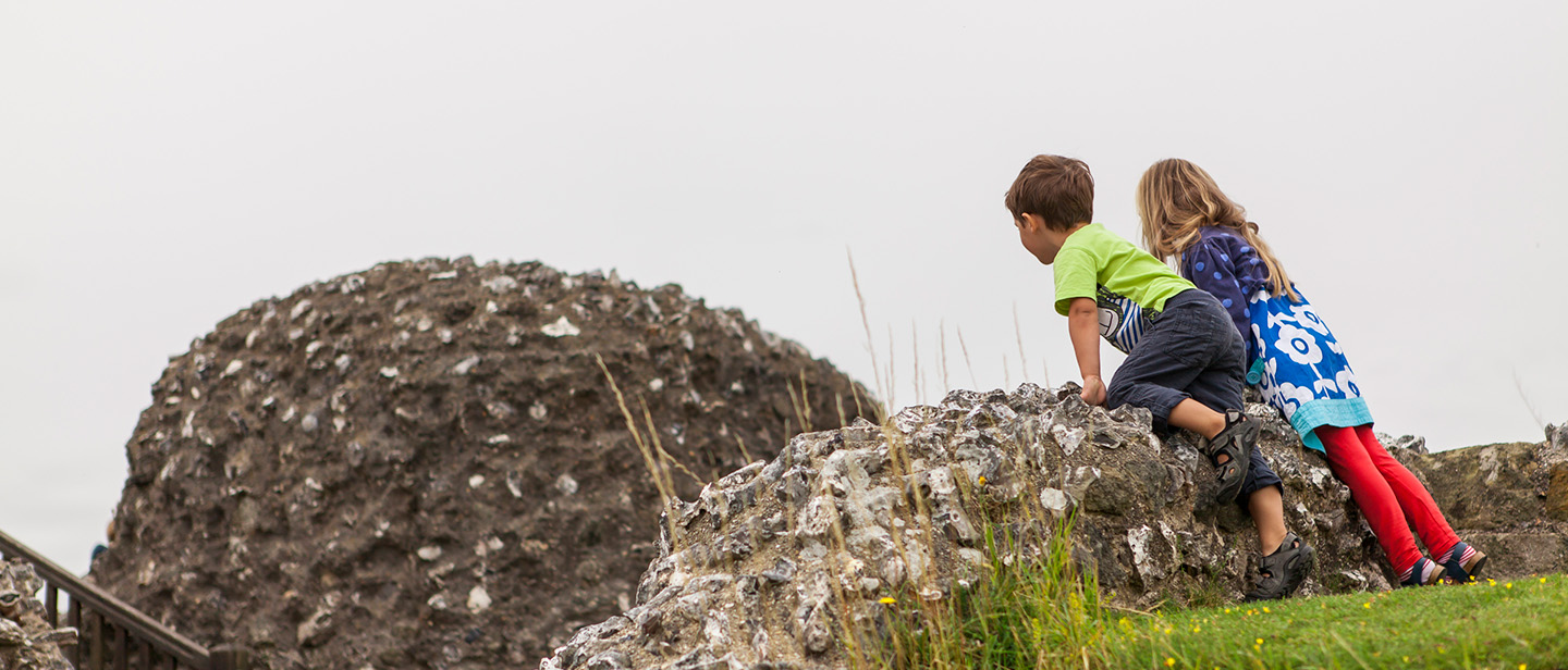 Photo of two young children looking out over the remains of stone walls at Old Sarum in Wiltshire on a cloudy day