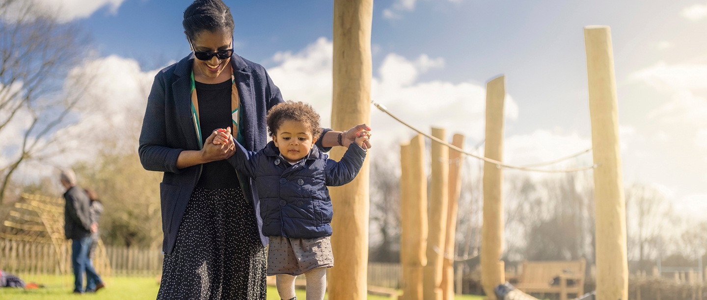 Photo of an adult helping a toddler to walk at the play area at Marble Hill in London on a sunny day