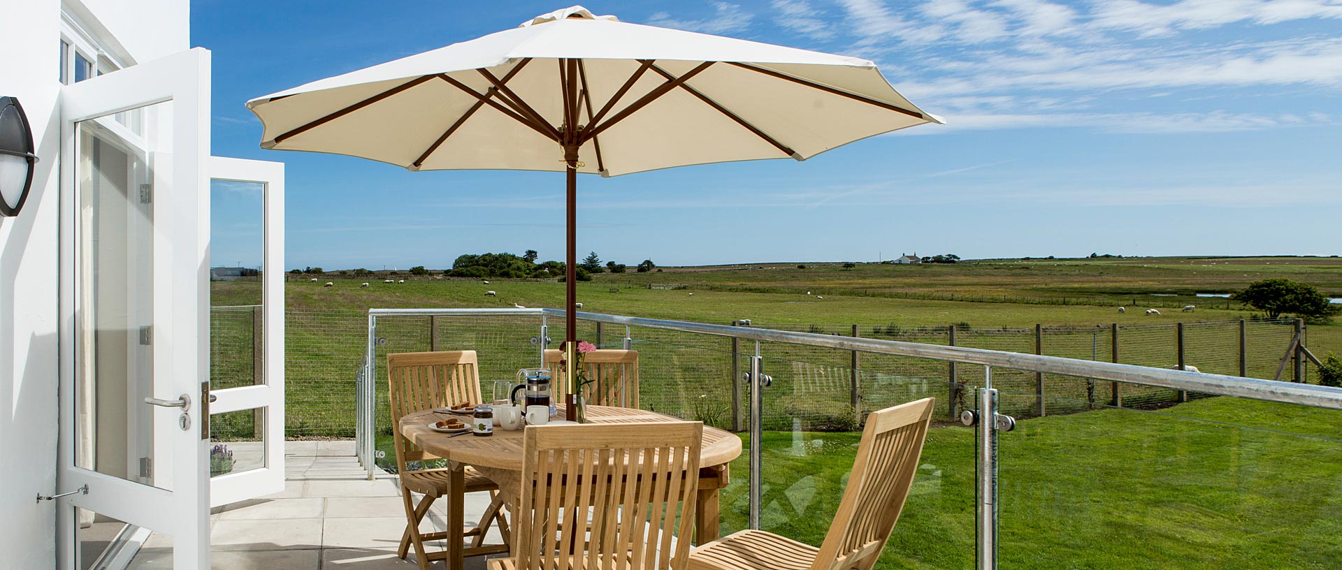 A table with parasol on a verandah looking across green fields