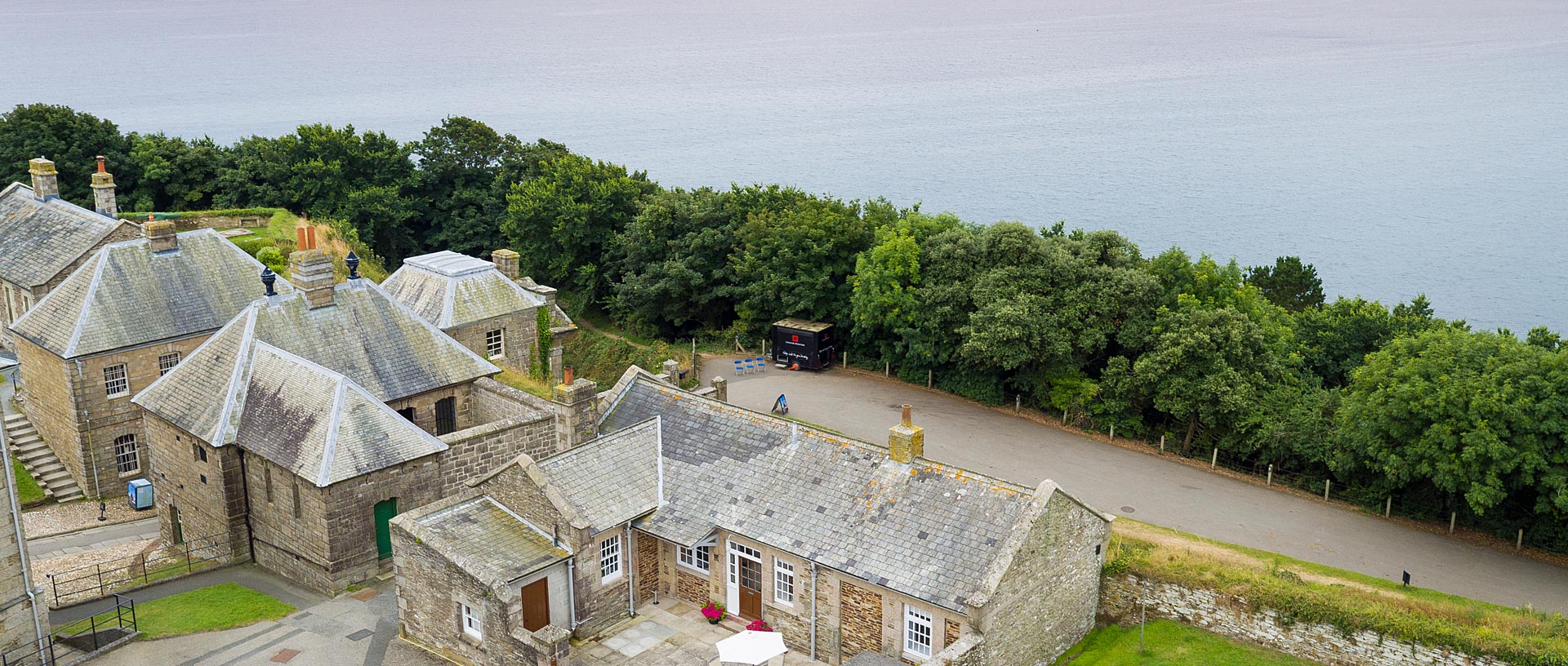 An aerial view of an old military building turned cottage with trees and the sea beyond