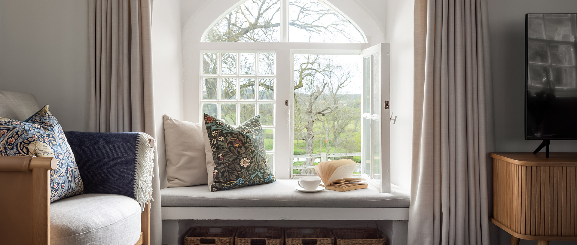 An open bay window in a living room overlooking trees.