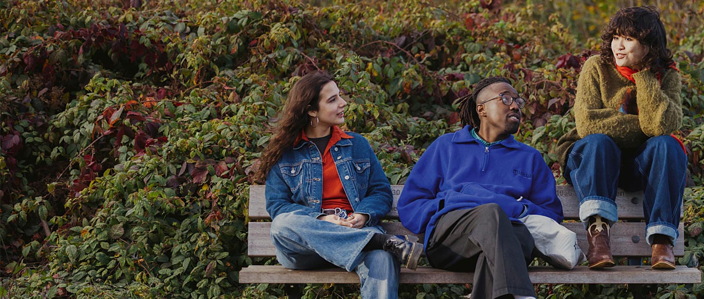 Three people sit on a bench chatting