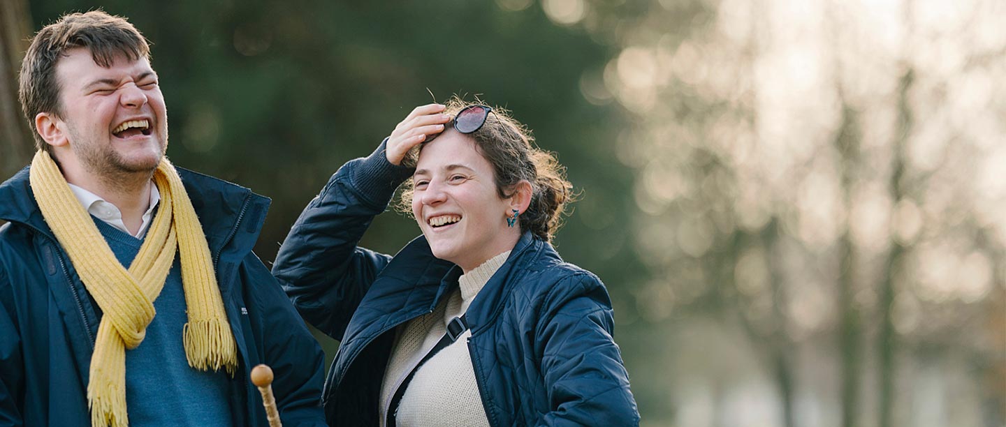 A man and a woman laugh in an autumnal looking woodland