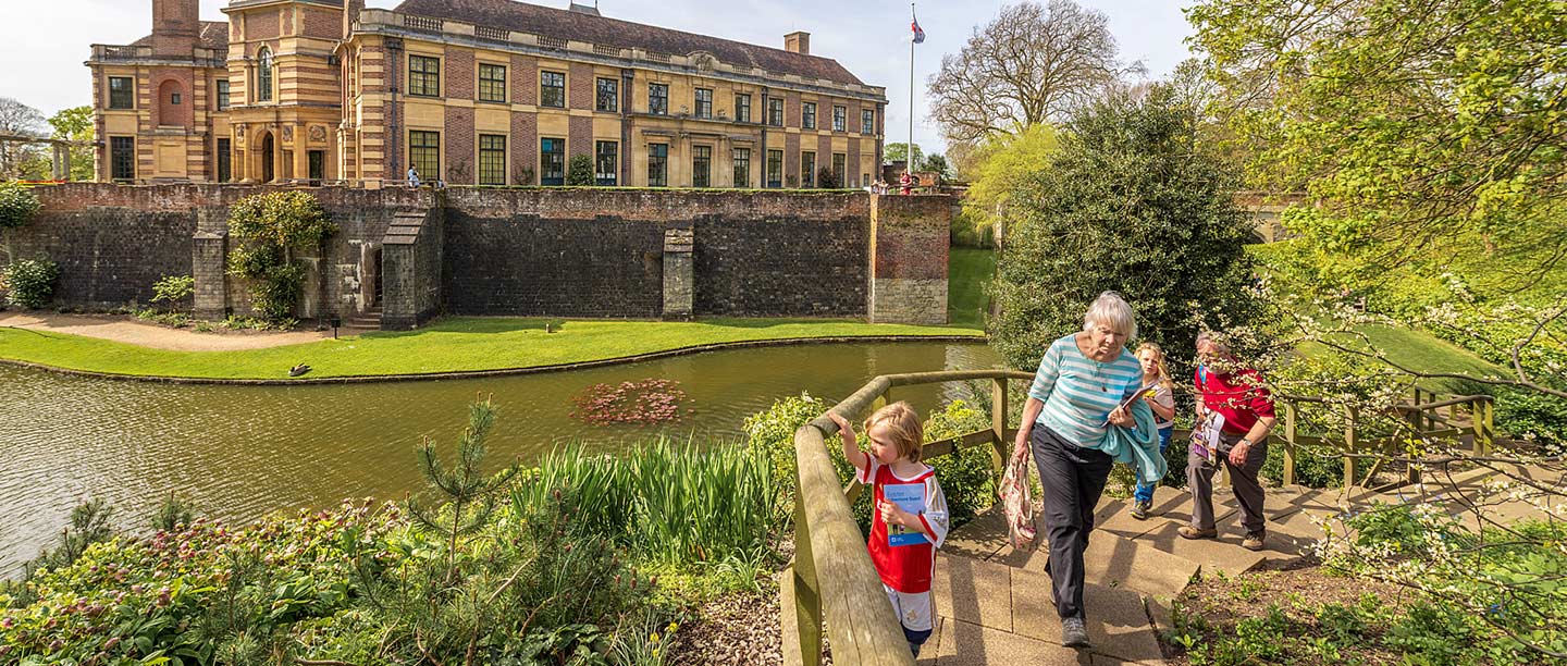 A woman, man and two children walk along a path with a large palace behind