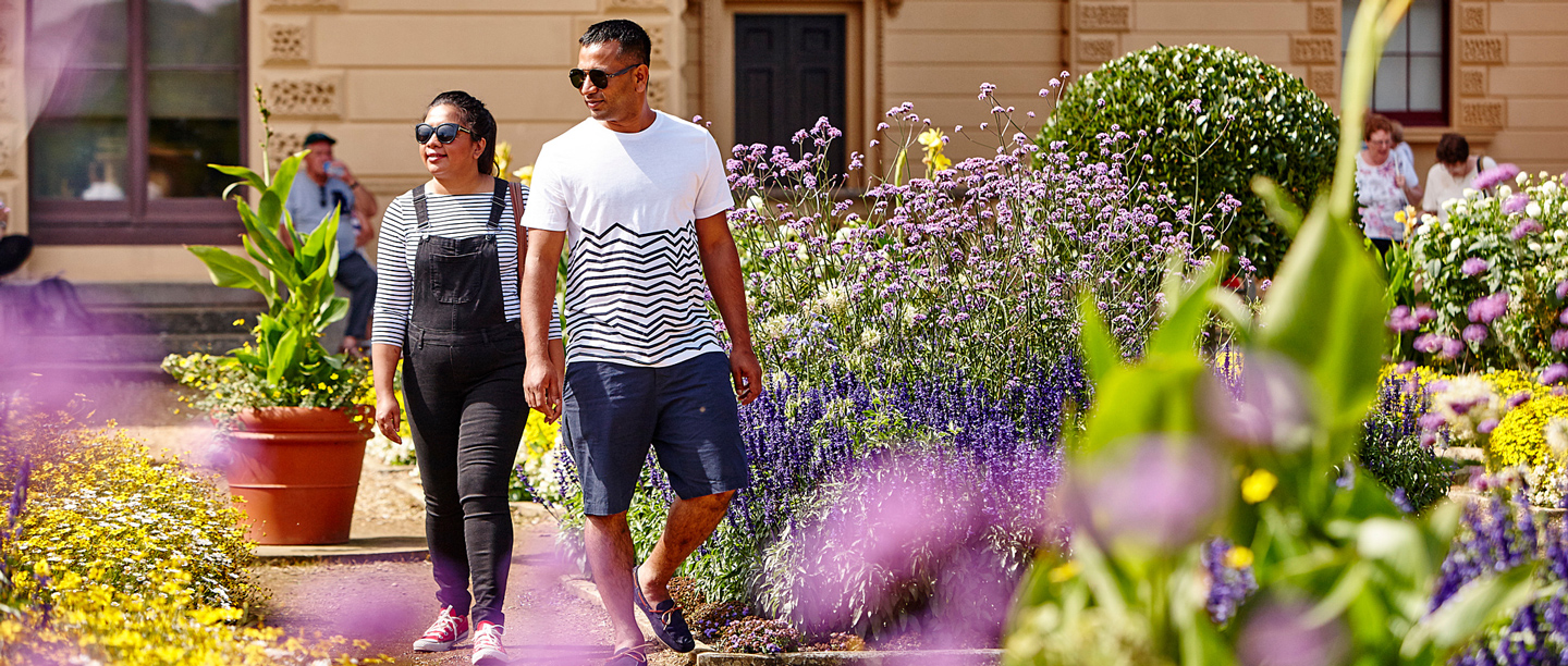 Two people walk through the flower beds in the gardens at Osborne on a sunny day.