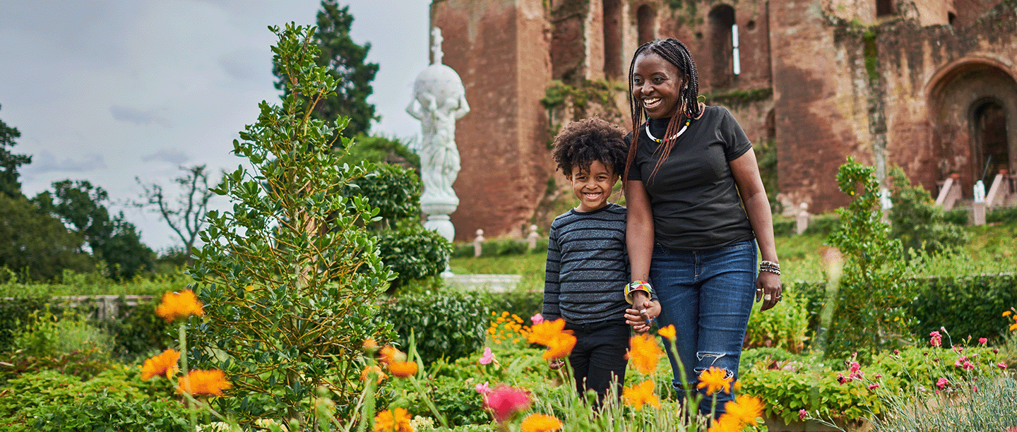 Photo of an adult and a child walking through the colourful Elizabethan Garden with Kenilworth Castle in the background