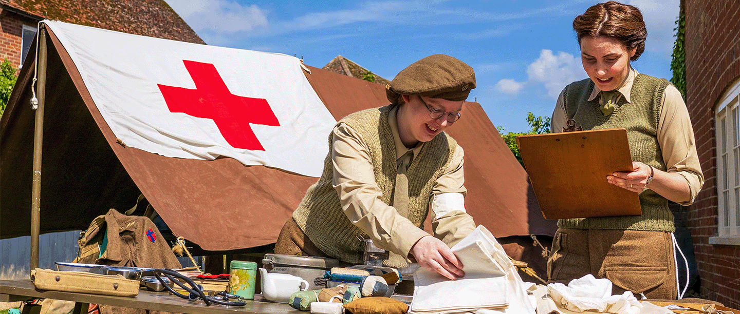 Photo of two people dressed in Second World War clothing arranging medical items from the period on a table