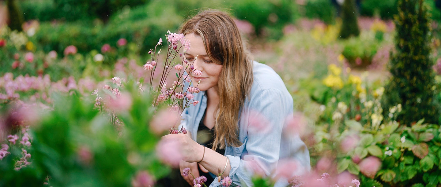 A woman kneels to smell the flowers in the flower beds at Kenilworth Castle's Elizabethan Gardens.