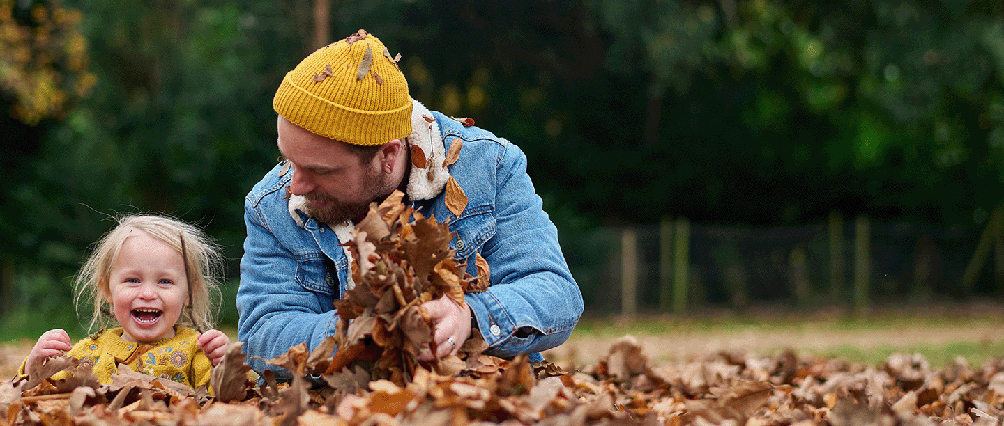 Photo of a young child and an adult sitting in a deep pile of autumn leaves and laughing