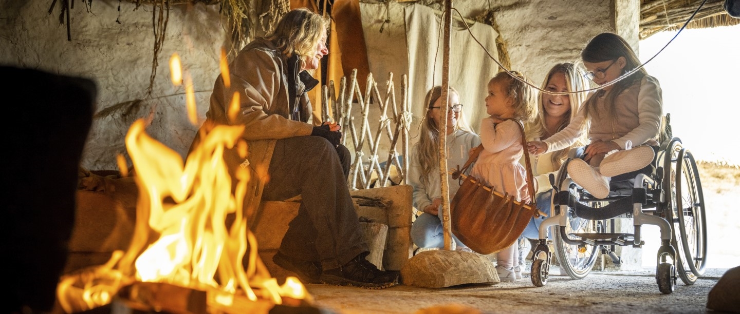 Image: Photo of people sat around a fire in a recreated Neolithic house at Stonehenge