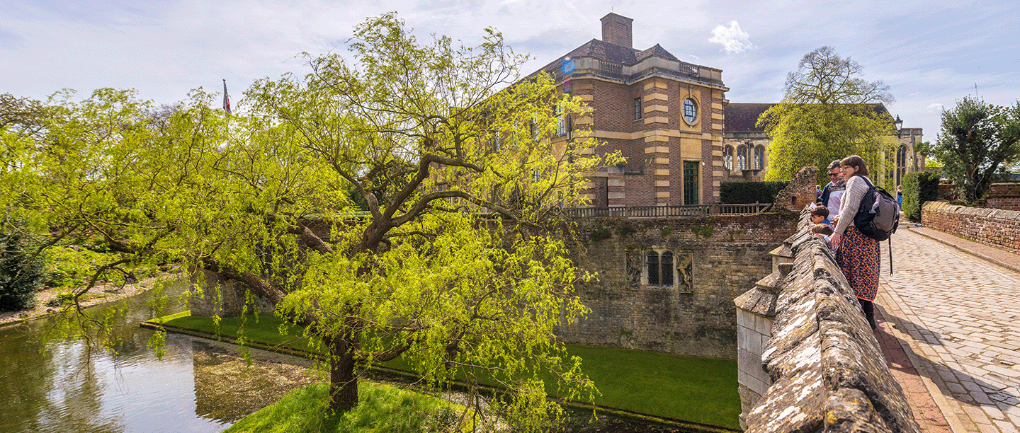 Photo of two adults and two children looking out over the moat at Eltham Palace on a sunny day