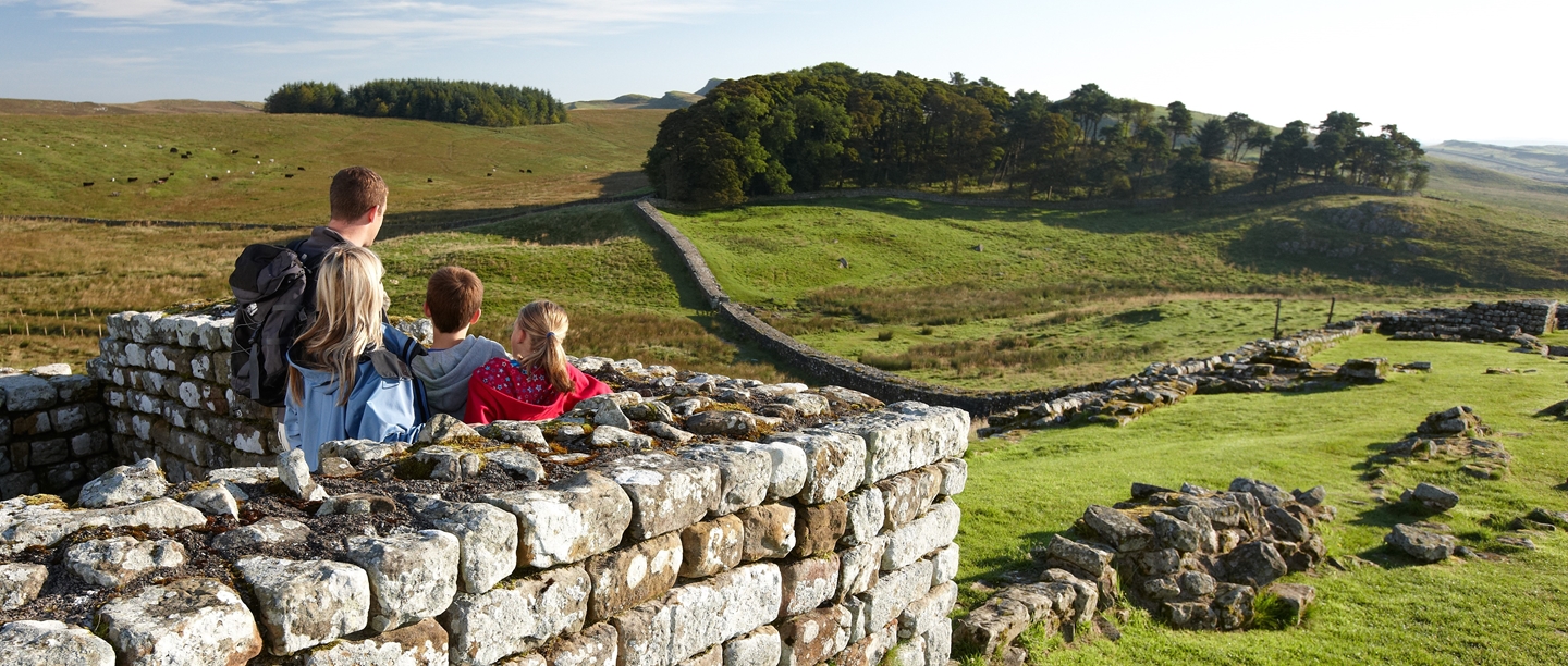 Photo of an adult and three children looking out along Hadrian's Wall in the autumn