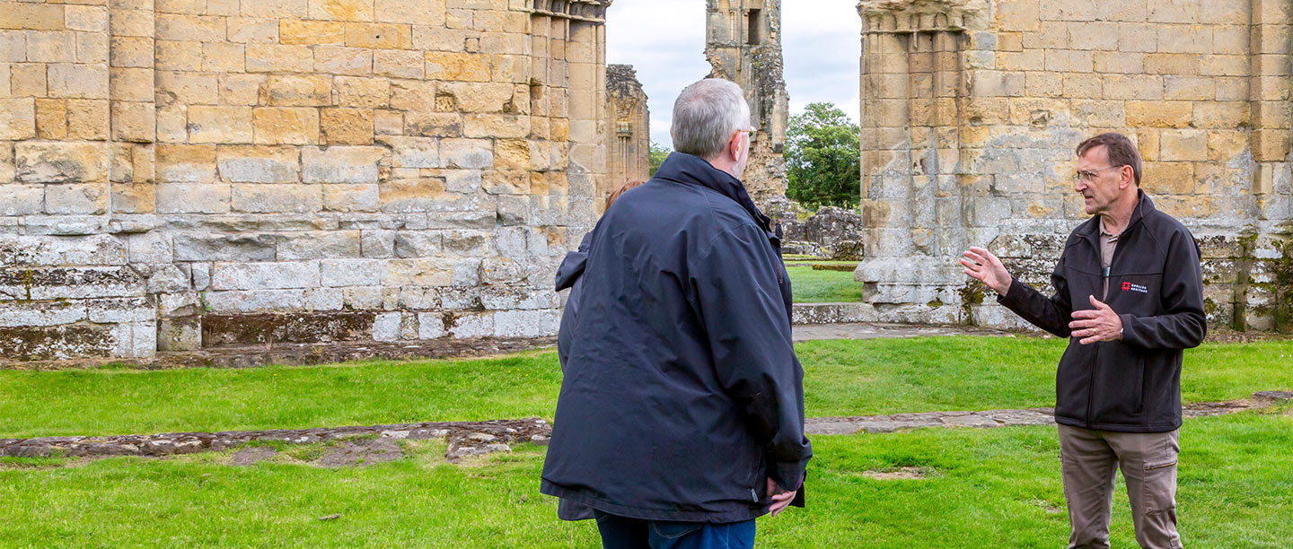An English Heritage volunteer shows some visitors around a ruined Byland Abbey