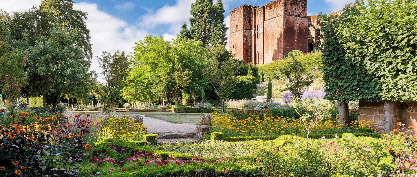 Photo of a small formal garden in bloom at Kenilworth Castle and Elizabethan Garden in Warwickshire, with the medieval Great Tower in the background