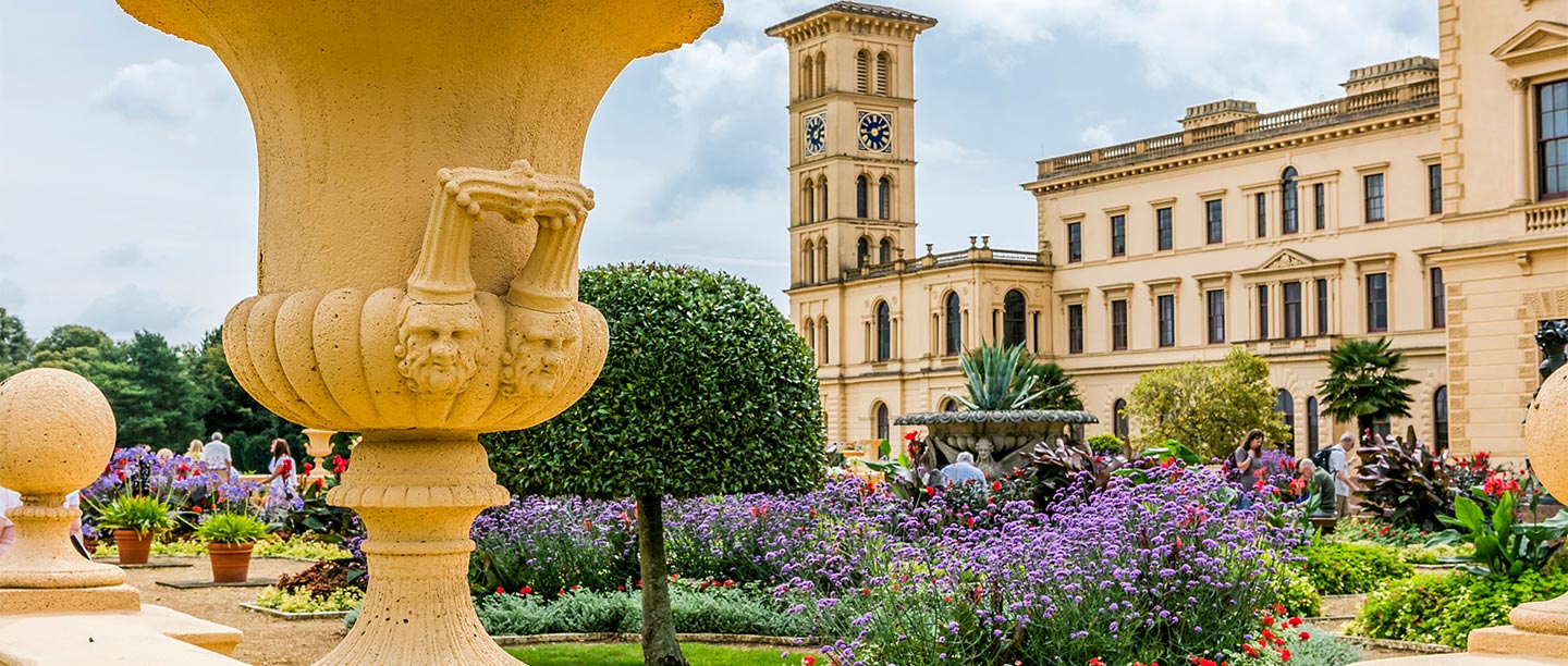 A large palatial house seen beyond a colourful flowerbed