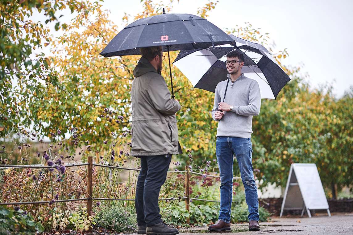 Image: Staff member talks to a visitor beneath umbrellas at Wrest Park