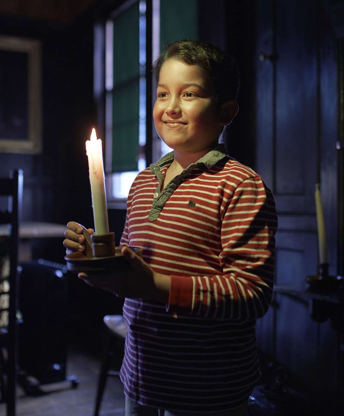 Image: A child carrying a candle in the dark at Boscobel House
