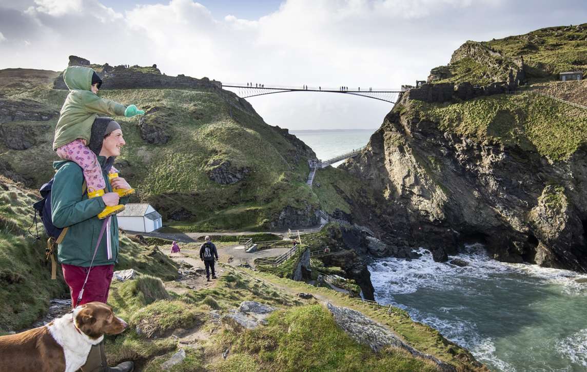 Image: A family look out at the water and bridge at Tintagel Castle Image: A family look out at the water and bridge at Tintagel Castle