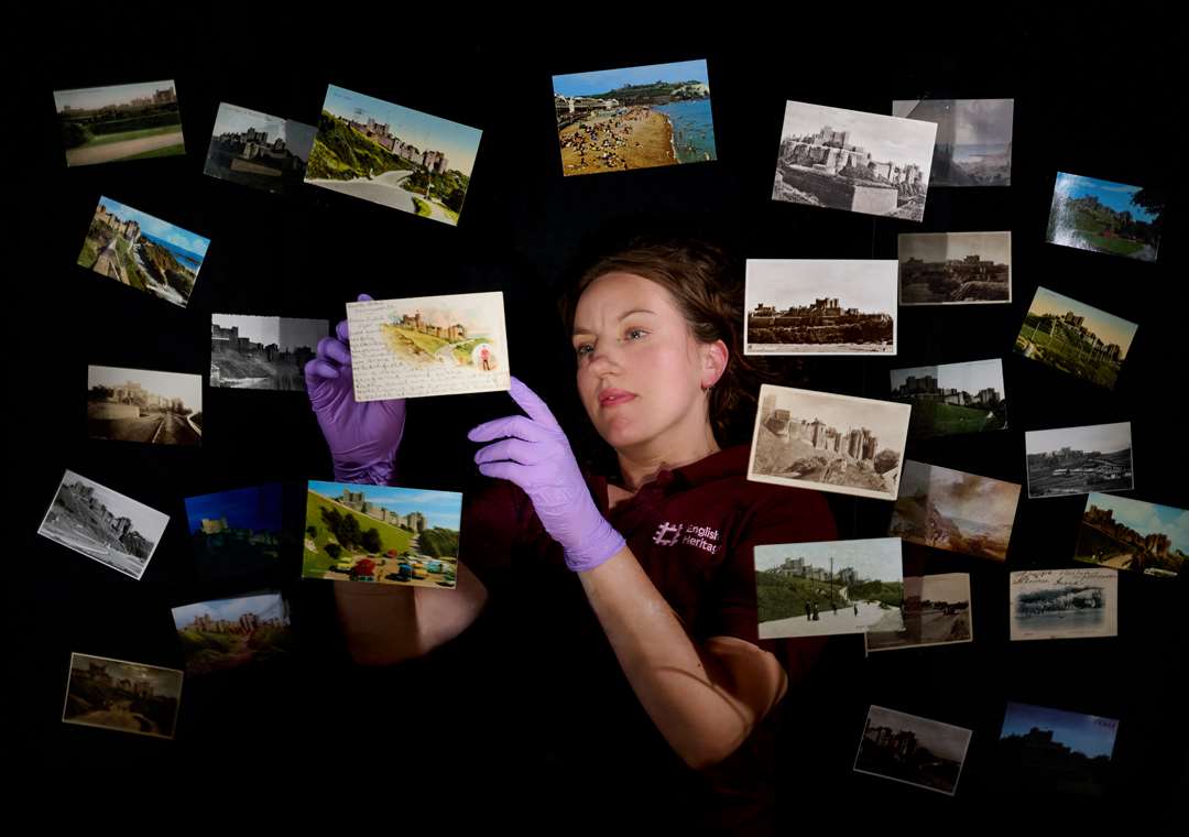 A large selection of postcards on a black background. A woman wearing purple latex gloves holds a postcard up. A large selection of postcards on a black background. A woman wearing purple latex gloves holds a postcard up.