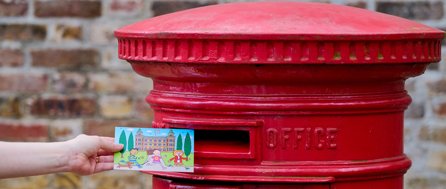 A colourful postcard is just about to be put into a red letterbox