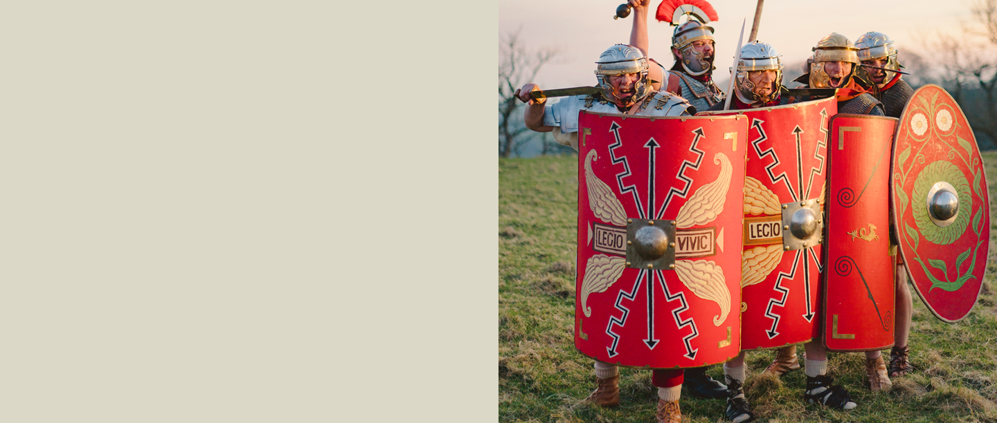 Image: Re-enactors dressed as Roman soldiers in full armour with red shields and socks on with their sandals