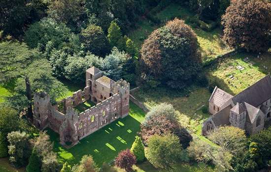 Aerial view of Acton Burnell Castle ruins alongside 13th century medieval St Mary's Church set amongst a rich planting of trees