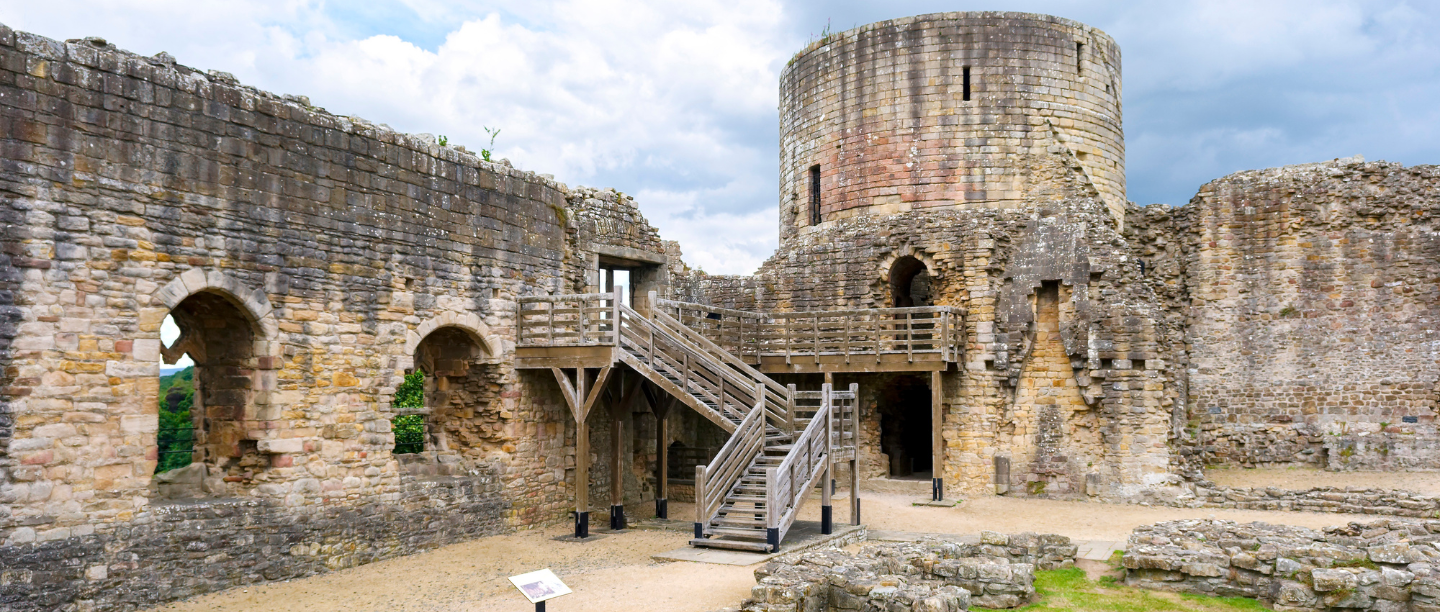 A view of the stone wall ruins of Barnard Castle with a wooden bridge.