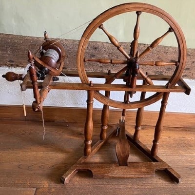 An antique, wooden spinning wheel, being used to spin fleece into yarn.