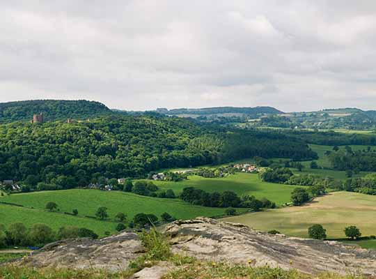 The view from the inner ward is one of the most dramatic in Cheshire, looking over the cliff-edge of Pulpit Rock to the hills of Wales (in the background), with the mid-Cheshire idge in the middle ground and former medieval open fields in the foreground. Peckforton Castle stands to the left