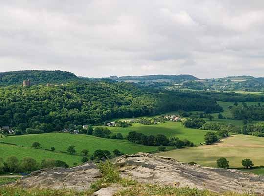 The view from the inner ward is one of the most dramatic in Cheshire, looking over the cliff-edge of Pulpit Rock to the hills of Wales (in the background), with the mid-Cheshire idge in the middle ground and former medieval open fields in the foreground. Peckforton Castle stands to the left