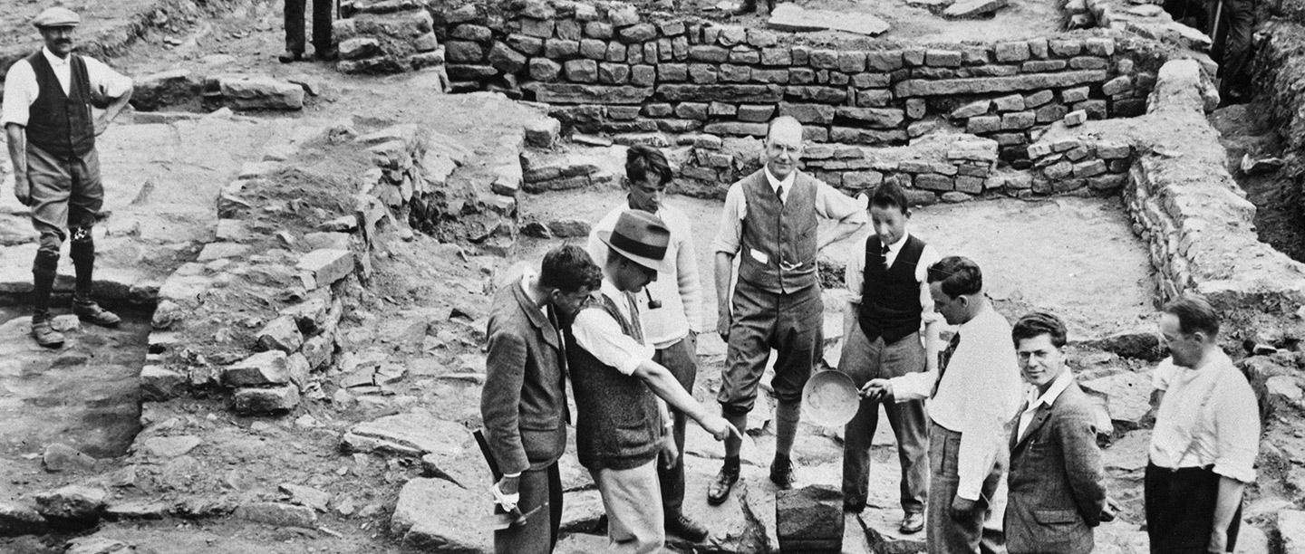 Black and white photograph showing archaeologists grouped around a piece of Roman stone