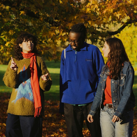 Three young people chat as they walk through an autumnal landscape.