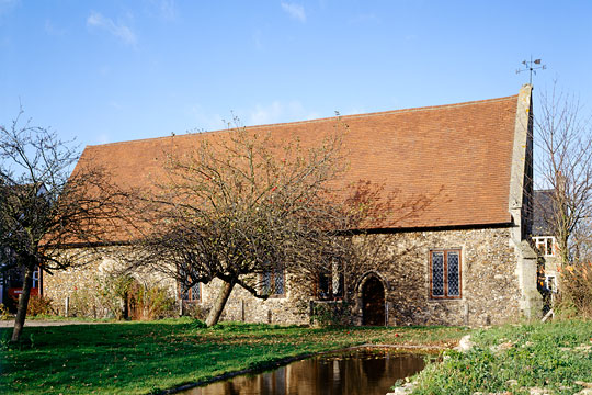 An outside view of Duxford Chapel with a weather vane on the apex of the roof gable end