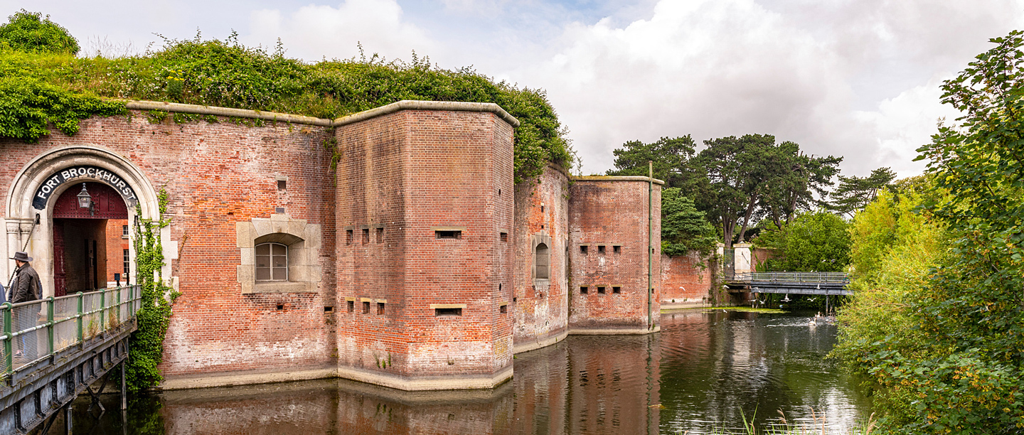 A view of the brick walls at Fort Brockhurst with a man standing on the bridge over the water.