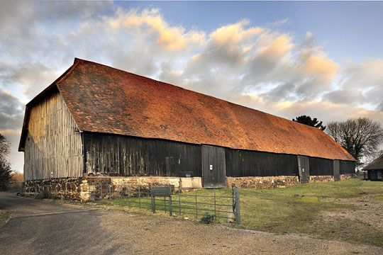 Harmondsworth Barn from the south-east with red roof tiles catching the sun and a dramatic sky above