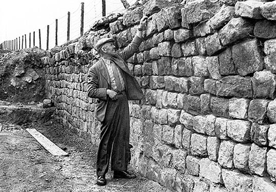 Black and white photogarph of Charles Anderson inspecting the Wall east of Birdoswald
