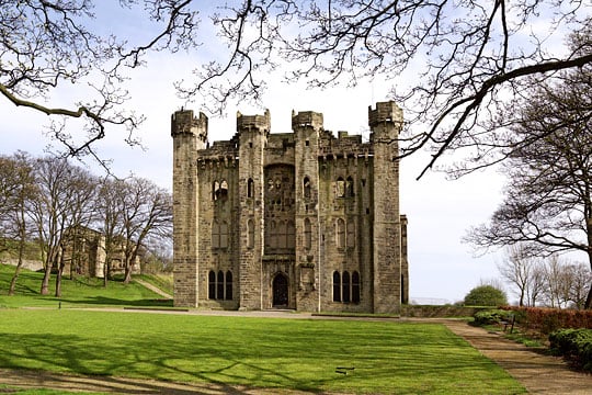 Hylton Castle, an imposing stone edifice surrounded by lawn and trees with the remains of St Catherinw's Chapel in the background