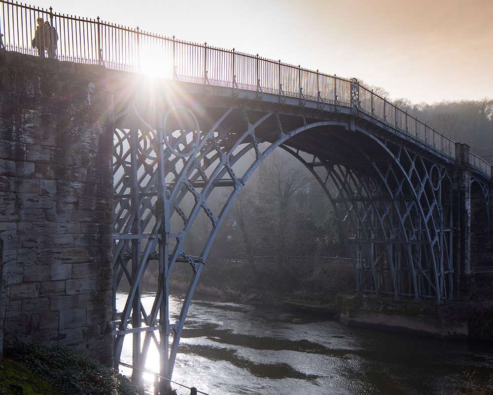 Visitor walking across the Iron Bridge with sun shining through the railings 