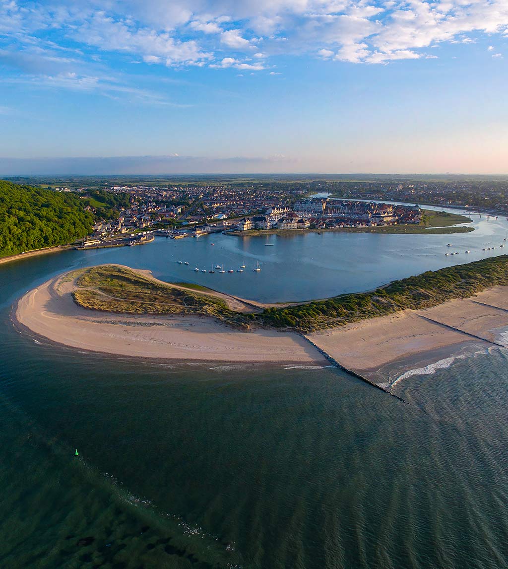 A wide river estuary, viewed from the air, showing a road on the left running towards a town on the far bank of the estuary and boats at anchor in the water