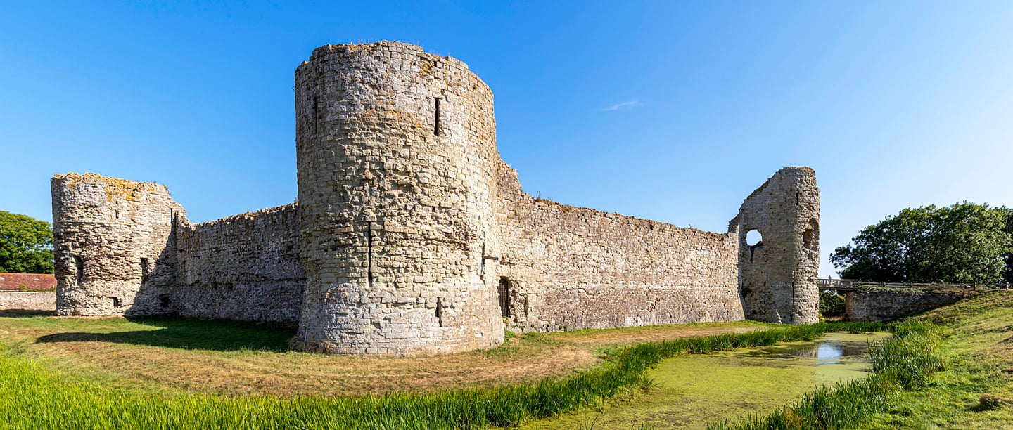 A view of the medieval ruins of Pevensey Castle and moat on a sunny day.