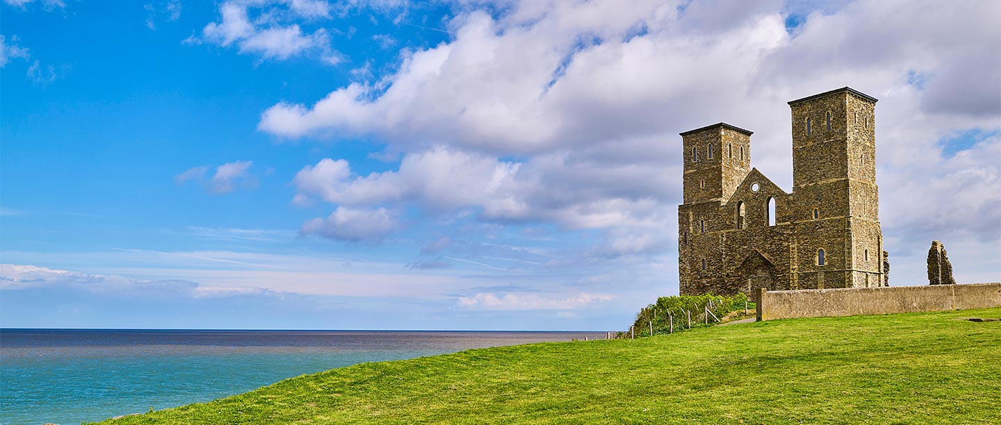 A ruined church front with two towers looks out across the sea