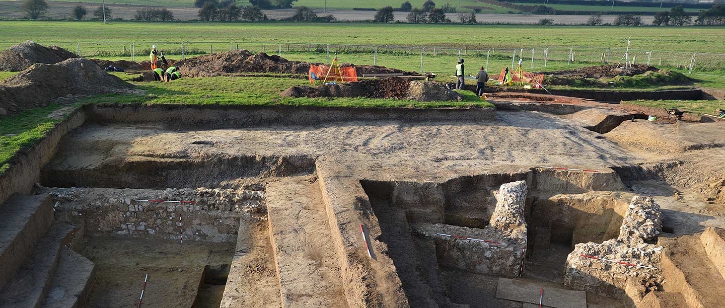 Excavations taking place at Richborough Roman amphitheatre.  Trenches in the foreground and people at work digging behind