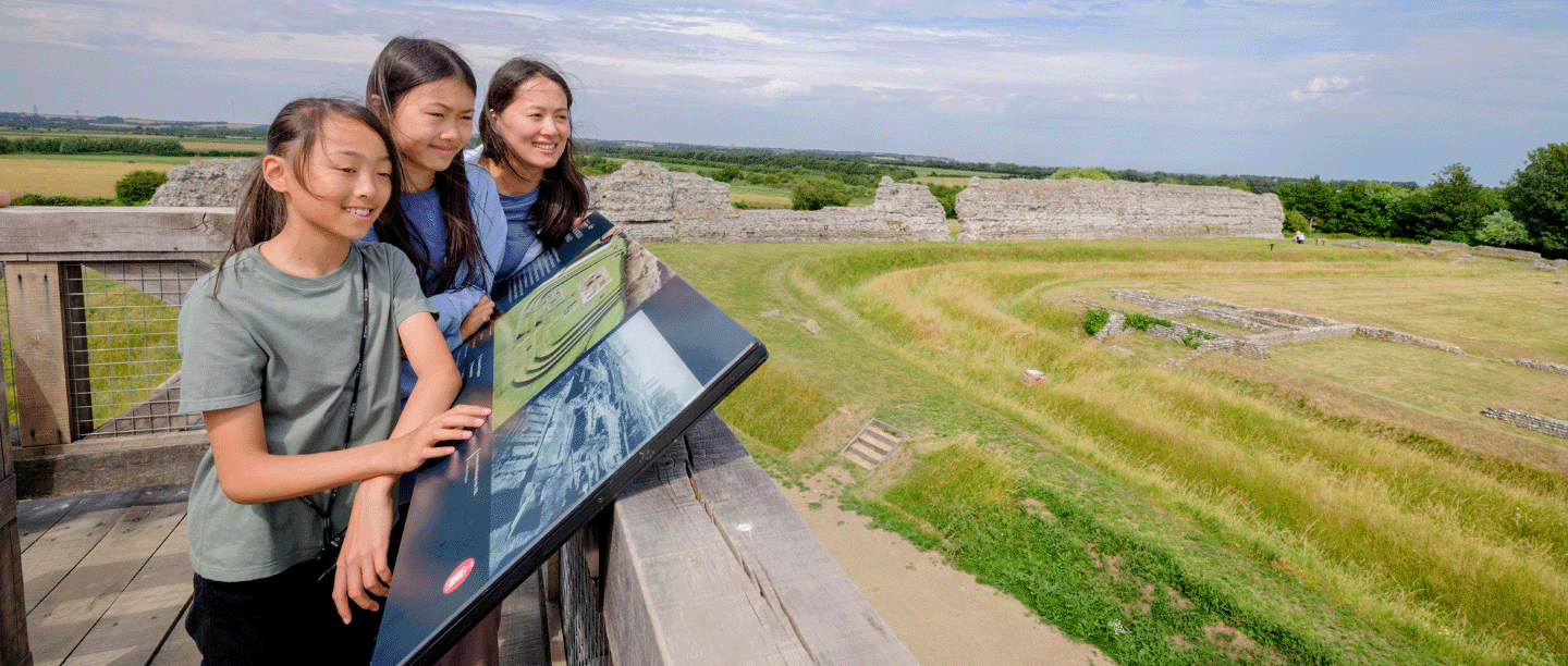 Photo of an adult and two children looking out over Richborough Roman Fort and Amphitheatre on a sunny day