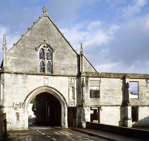 A grey building with a road passing through an arch in it and a recessed section above a small pedestrian door to the left