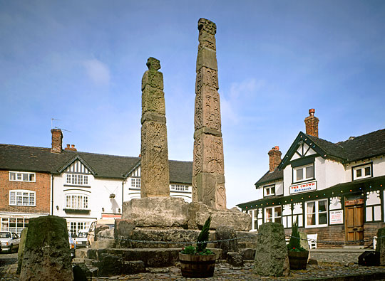 View of the intricately carved crosses at Sandbach in the Market Square with shops and restaurants behind