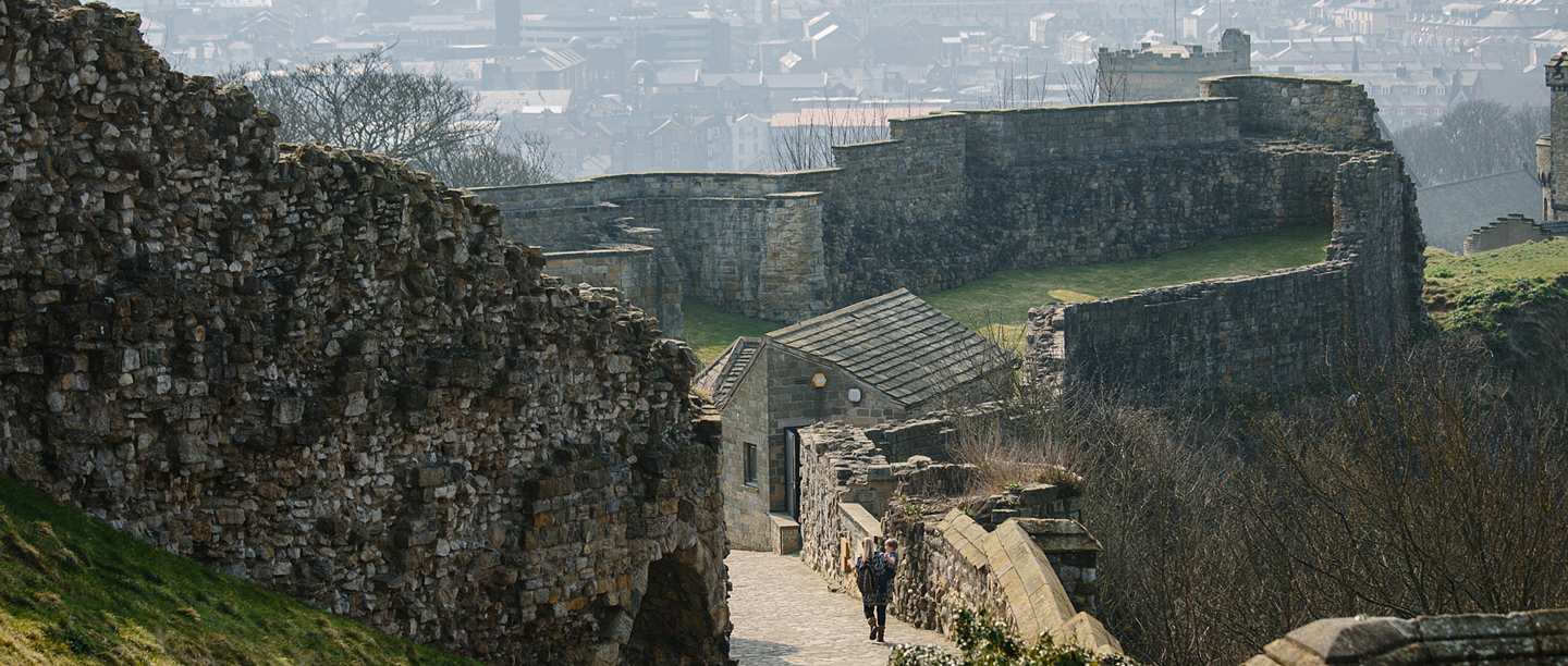 A view of the stone walls at Scarborough Castle with an adult walking down the path.