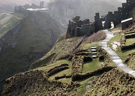 The remains of Tintagel Castle on Tintagel island, looking towards the mainland. There is a path running through it. To the left of the path are some of the remains of the 5th- to 7th-century settlement The remains of Tintagel Castle on Tintagel island, looking towards the mainland. There is a path running through it. To the left of the path are some of the remains of the 5th- to 7th-century settlement