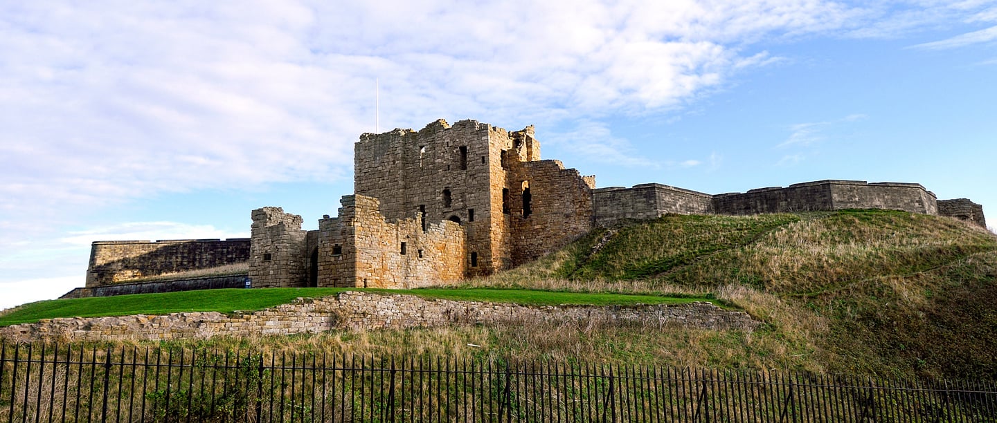A low angle view of Tynemouth Priory on top of a hill.